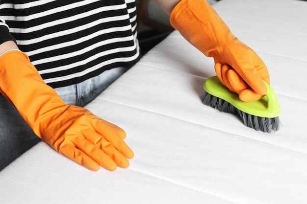 Vrouw in oranje handschoenen die witte matras met borstel binnen close-up schoonmaken