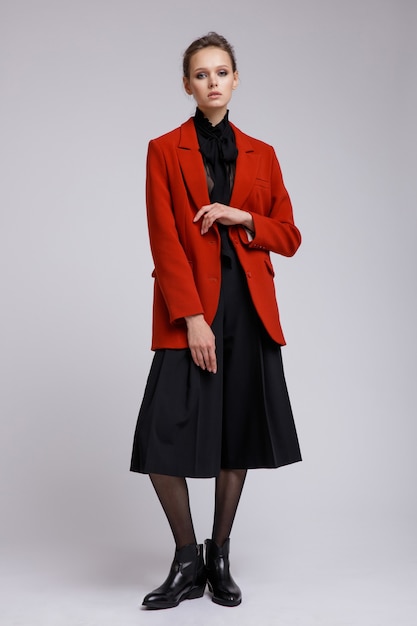 Vrouw in pak rood jasje zwarte transparante blouse korte broek op witte zachte grijze achtergrond