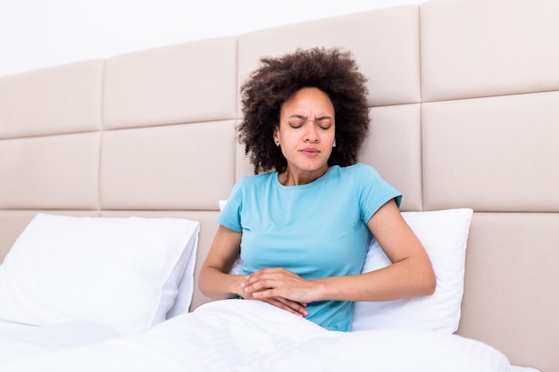 Vrouw in pijnlijke uitdrukking die handen houden tegen buik die aan menstruatiepijn lijden, droevig liggend op huisbed