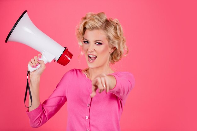 Vrouw in pin-up stijl schreeuwen in megafoon geïsoleerd op roze achtergrond studio portret meisje pointi...