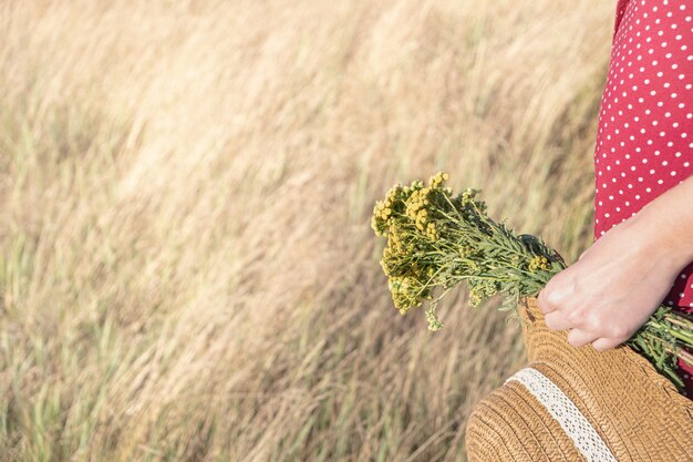 vrouw in polka-dot jurk met boer hoed en boeket bloemen in haar hand