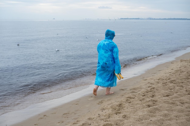 Vrouw in regenjas die op het strand loopt