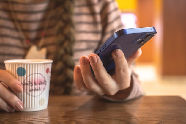 Vrouw in restaurant met behulp van moderne mobiele telefoon in de hand met koffiekopje op een houten tafel communicatie...