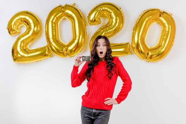 Vrouw in rode het malplaatjecreditcard van de sweaterholding voor 2020 nieuwe jaarballons