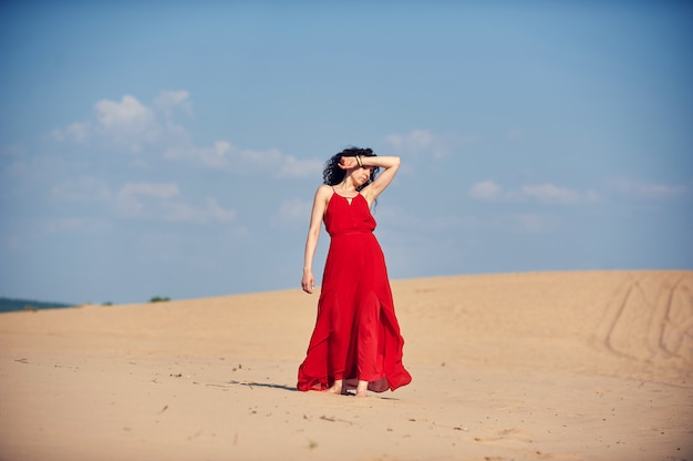 Vrouw in rode jurk dansen in de woestijn op blauwe hemel