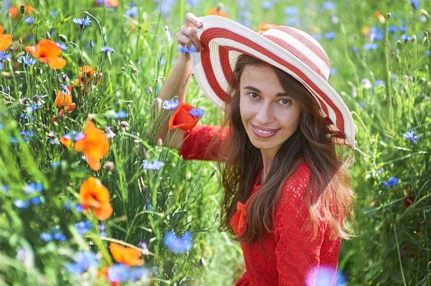 vrouw in rode jurk en een grote rode gestreepte hoed zitten in een prachtig bloeiende klaproos veld