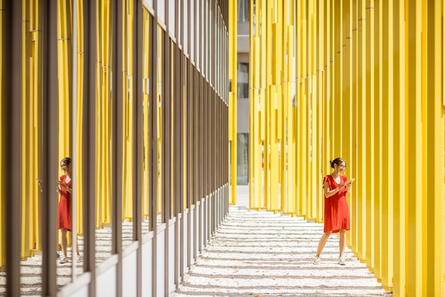 Vrouw in rode jurk op de moderne gele muur achtergrond van het gebouw. Algemeen plan met abstracte geometrische compositie