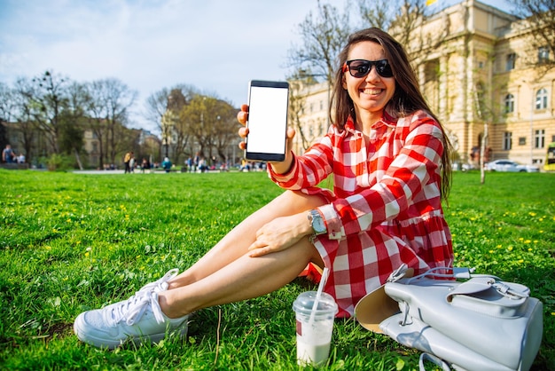 Vrouw in rode jurk zit in park met smartphone. toon kopieerruimte op telefoon