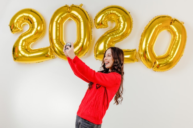Foto vrouw in rode sweater die foto's met uitstekende camera voor 2020 nieuwe jaarballons nemen