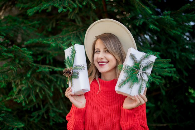 Vrouw in rode sweater met Kerstmisgiften dichtbij pijnboomboom