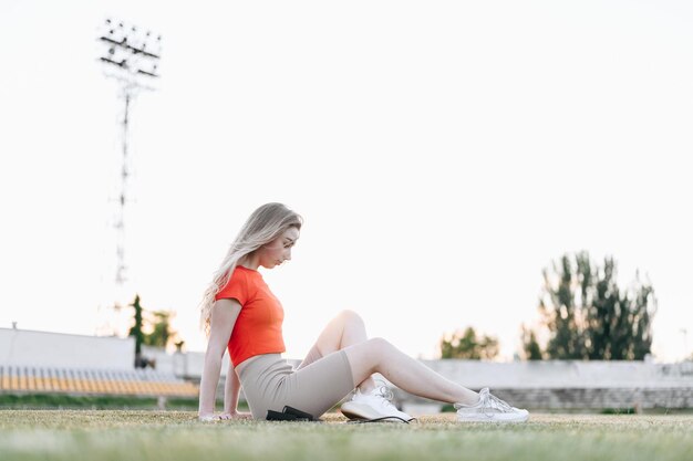 Vrouw in rode top zit op stadion bij zonsondergang tegen Sun Girl-oefeningen op zomeravond