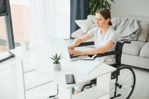 Vrouw in rolstoel werkt op de laptop in het thuiskantoor met een hulphond als begeleider