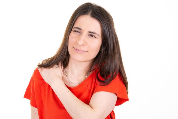 Vrouw in rood shirt met pijn met hoofdpijn hand op schouder kijk kant op witte achtergrond