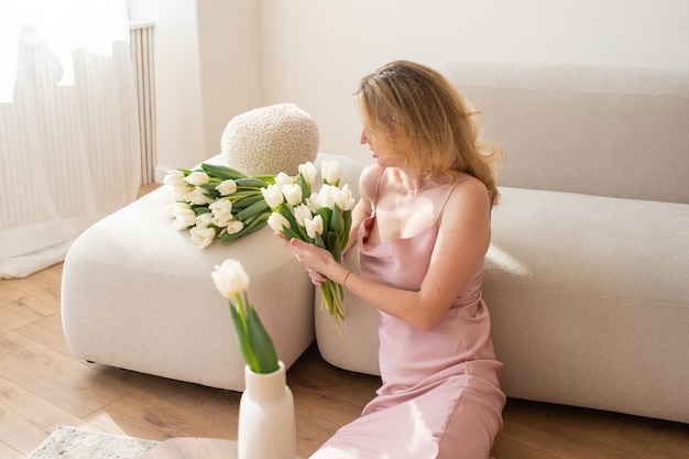 Vrouw in roze jurk met witte tulpen op beige bank