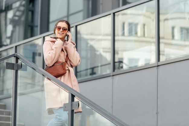 Vrouw in roze jurk praten met smarthone buiten op grijze stedelijke stad achtergrond