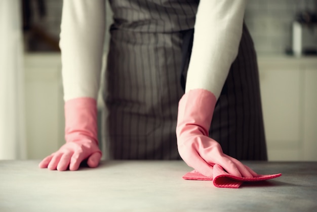 Vrouw in roze rubber beschermende handschoenen die stof en vuil afvegen.