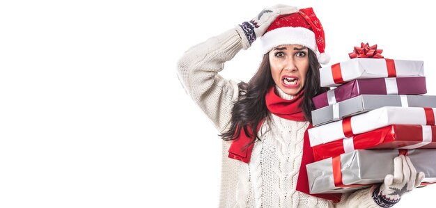 Vrouw in Santa's pet en witte zits op een witte achtergrond houdt kerstcadeautjes vast die gek worden van de seizoensdrukte.