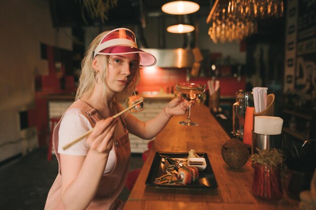 vrouw in schattige roze kleren eet sushibroodjes met stokjes drinkt wijn uit een glas