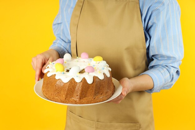 Vrouw in schort houdt paascake op gele achtergrond