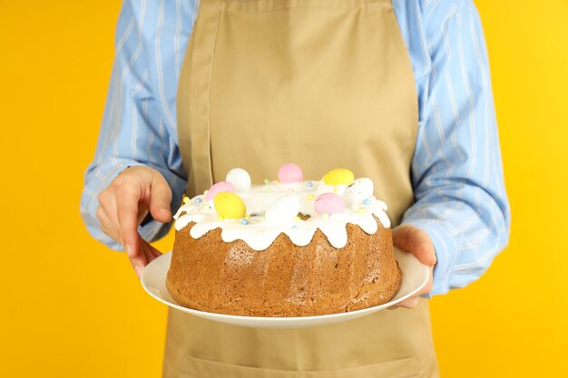 Vrouw in schort houdt paascake op oranje achtergrond