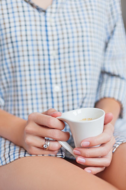 Vrouw in shirt zit op bed met een kop warme koffie