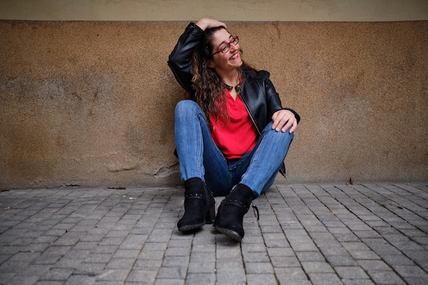 Vrouw in spijkerbroek en rood shirt zittend op straat