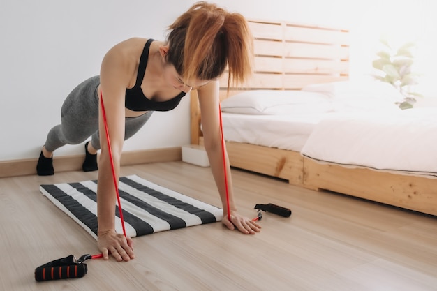 Vrouw in sport draagt doet weerstandsband push-up training in haar kamer