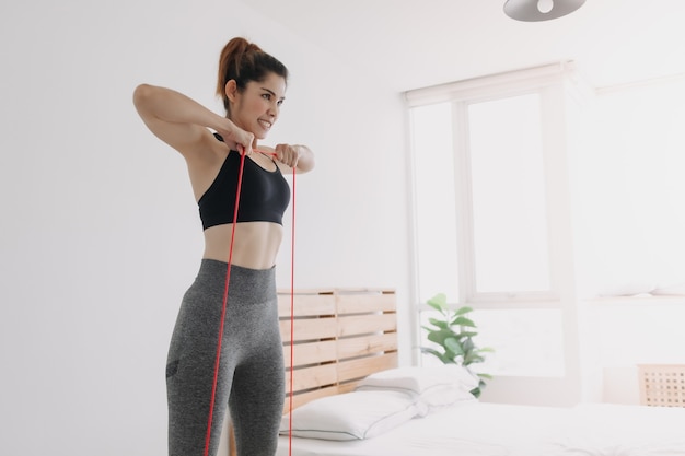 Vrouw in sport draagt weerstandsband rechtop rijtraining in slaapkamer