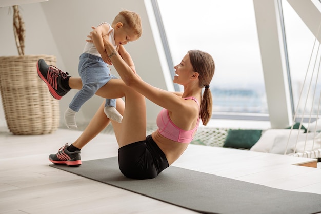 Vrouw in sportkleding die op een sportmat zit en een kind vasthoudt