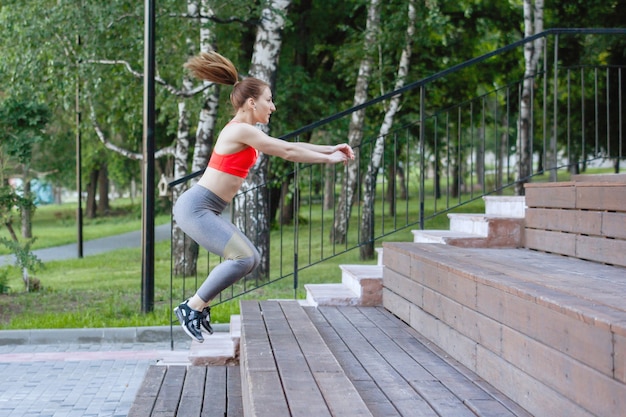 Vrouw in sportkleding squats op de houten treden van de trap in een stadspark in de zomer.