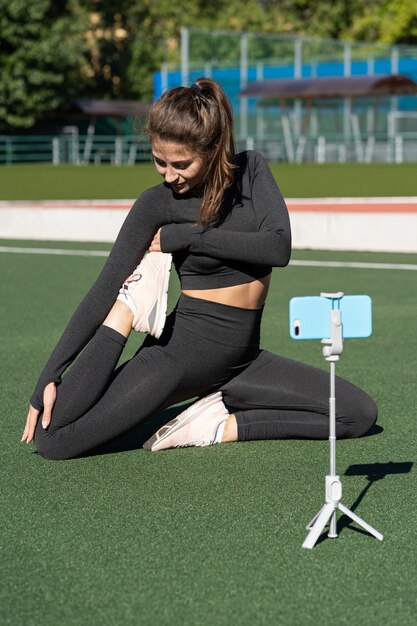 Vrouw in sportkleding vlogger zittend in een yoga-pose op kunstgras buiten