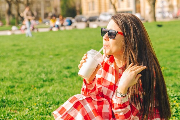 Vrouw in stadspark zittend op de grond en smoothie drinken