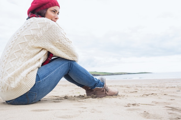 Vrouw in stijlvolle warme kleding zittend aan het strand