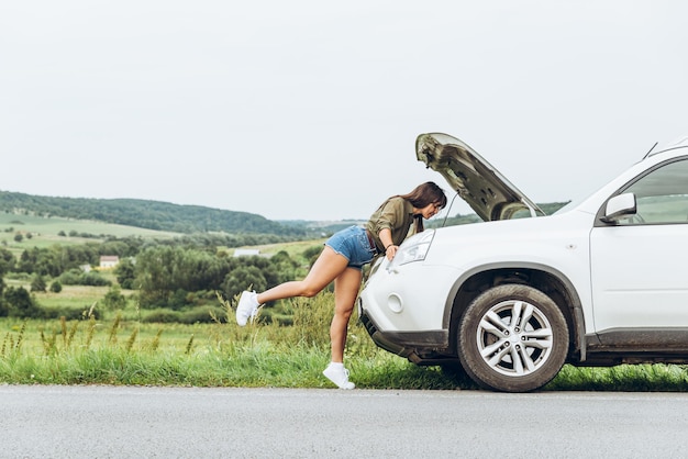 Vrouw in strakke shirts nieuwe kapotte auto met geopende motorkap