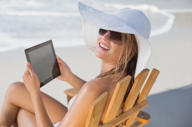 Vrouw in strohoed het ontspannen in ligstoel op het strand die tabletpc op een zonnige dag met behulp van