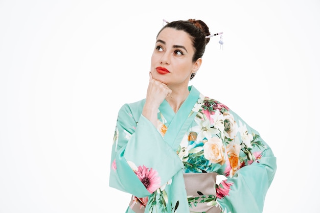 Vrouw in traditionele Japanse kimono kijkt omhoog met een peinzende uitdrukking die de hand op haar kin houdt en aan wit denkt