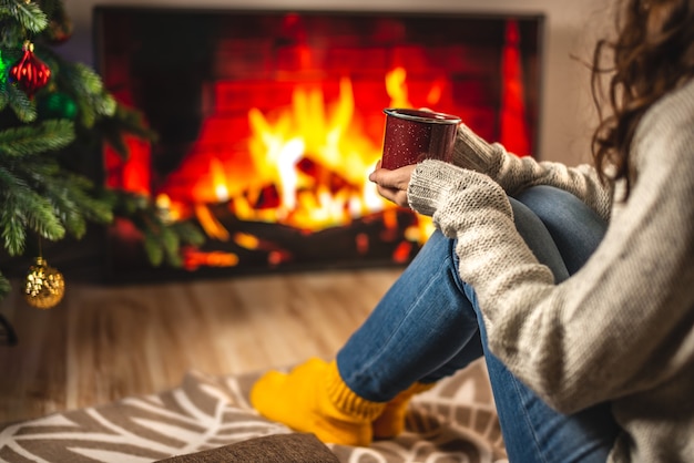 Vrouw in trui en warme sokken zit voor de open haard, die op het tv-scherm is afgebeeld