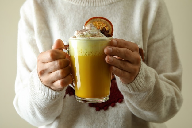 Vrouw in trui houdt glas pompoen latte vast