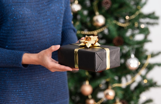 Vrouw in trui met geschenkdoos in de buurt van kerstboomachtergrond