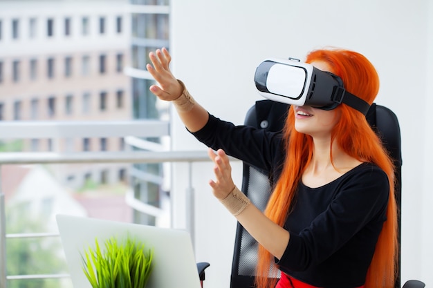 Vrouw in virtual reality headset wijzend in de lucht terwijl op haar werkplek op kantoor.