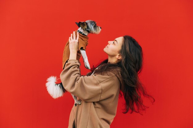 Vrouw in vrijetijdskleding geïsoleerd op rode achtergrond met hond in handen kijken naar pet