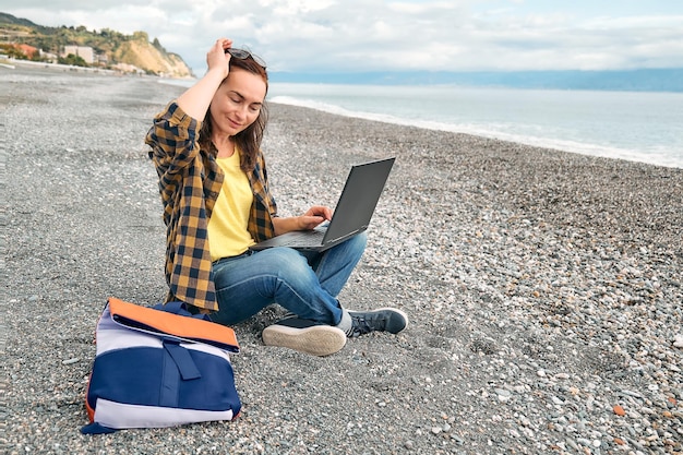 Vrouw in warm plaid shirt met laptop computer die buiten werkt terwijl ze op het winterstrand zit