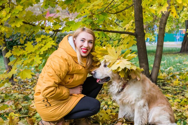 Vrouw in warme kleren met haar retriever in een herfstpark tussen gele bladeren.