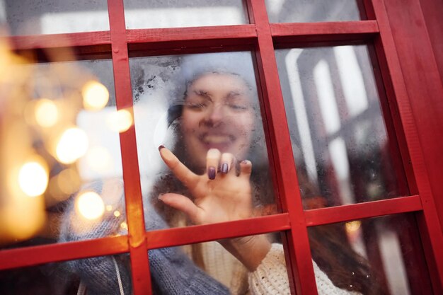 Vrouw in warme kleren veel plezier in het telefoonstation. Kijk door het glas.