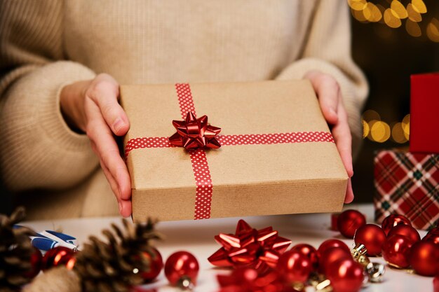 Vrouw in warme trui met geschenkdoos verpakt in ambachtelijk papier met feestelijk lint aanwezig voor winter