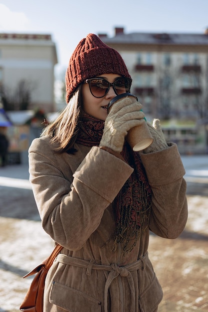 Vrouw in warme winterkleren en zonnebril die hete koffie drinken uit een papieren bekertje om mee te nemen