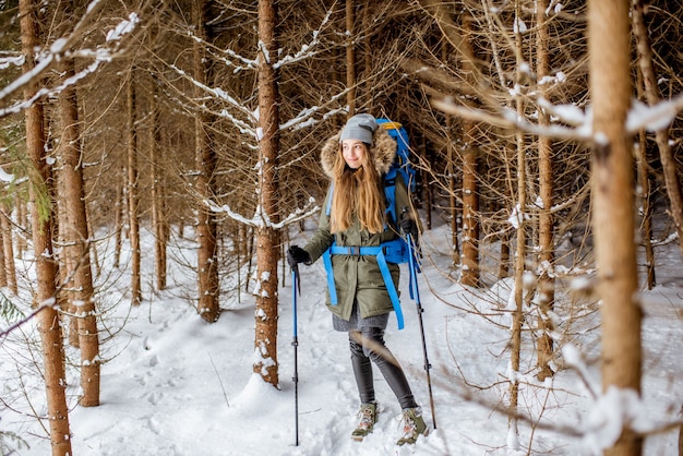 Vrouw in winterkleren wandelen met rugzak en volgstokken in het besneeuwde sparrenbos