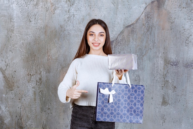 vrouw in wit overhemd met een zilveren geschenkdoos en een blauwe boodschappentas.