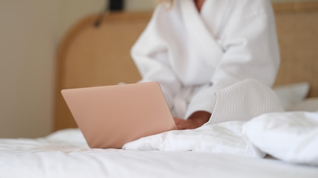 Vrouw in witte badjas zittend met laptop in bed thuis close-up