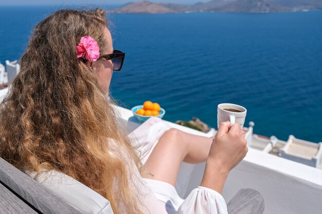 Vrouw in witte jurk en bloem in haar koffiekopje op wit terras balkon